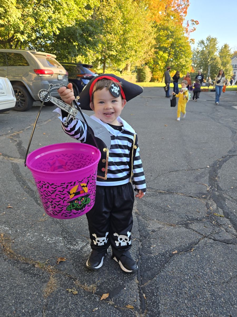 A smiling toddler dressed as a pirate holding up a purple treat bucket at the church Halloween event