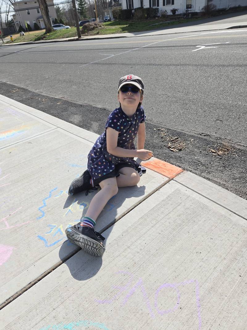 A child sitting on the sidewalk beside chalk drawings